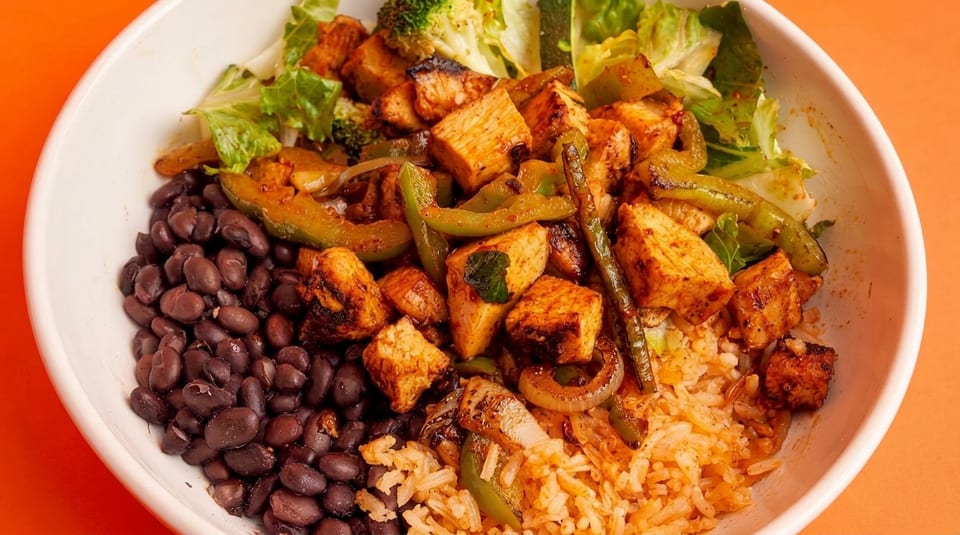 A vibrant bowl of rice, black beans, grilled tofu, green peppers, and lettuce.