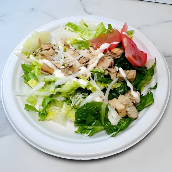 A chicken salad with lettuce, sliced tomatoes, onions, and white dressing on a white plate.