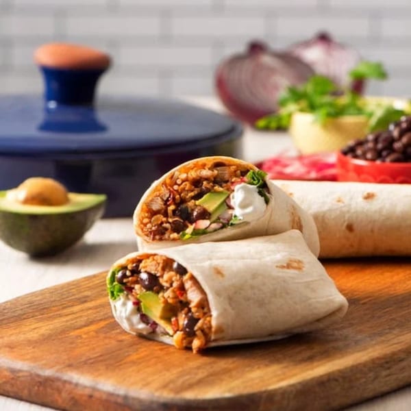Two gourmet burritos, one cut in half, filled with rice, beans, avocado, and sour cream.