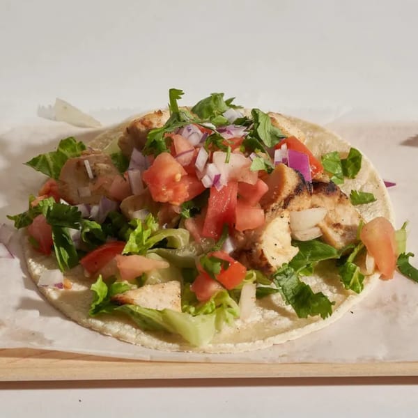 A chicken taco with lettuce, diced tomatoes, red onions, and cilantro on a white tortilla.
