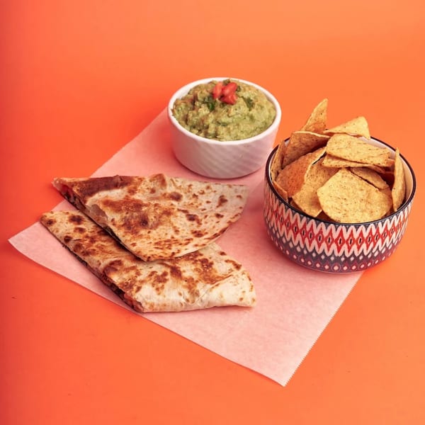 Quesadillas, guacamole, and tortilla chips on a vibrant orange background, from 360 Gourmet Burritos.
