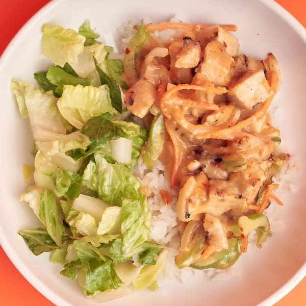 A white bowl filled with rice, chicken in a creamy sauce, and a side of fresh lettuce.