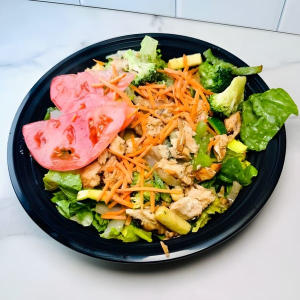 A vibrant salad with chicken, lettuce, broccoli, carrots, and tomato slices in a black bowl.