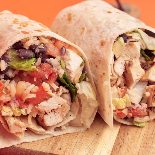 Two 360 Gourmet Burritos, filled with chicken, rice, black beans, lettuce, and tomatoes, on a wooden board.