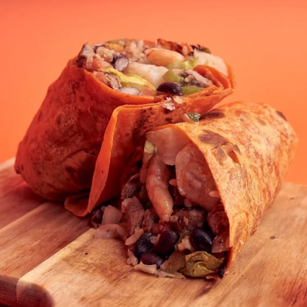 Two gourmet burritos, one cut open to reveal shrimp, black beans, and rice, on a wooden board.